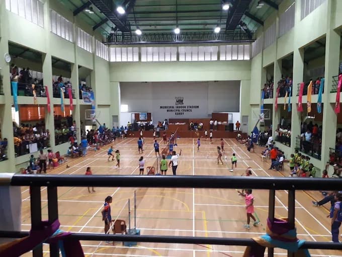 Junior tournament under way on the wooden floor at Kandy Municipal Indoor Stadium, several courts in play at once, seen from a packed first-floor spectator gallery