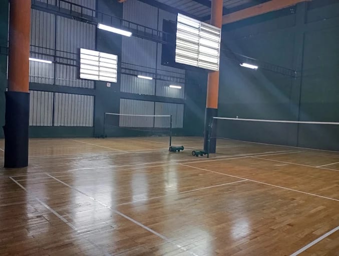 Two wooden badminton courts with nets up at Tamil Union, Colombo 08, dark green walls and structural pillars beside the court under louvred lighting