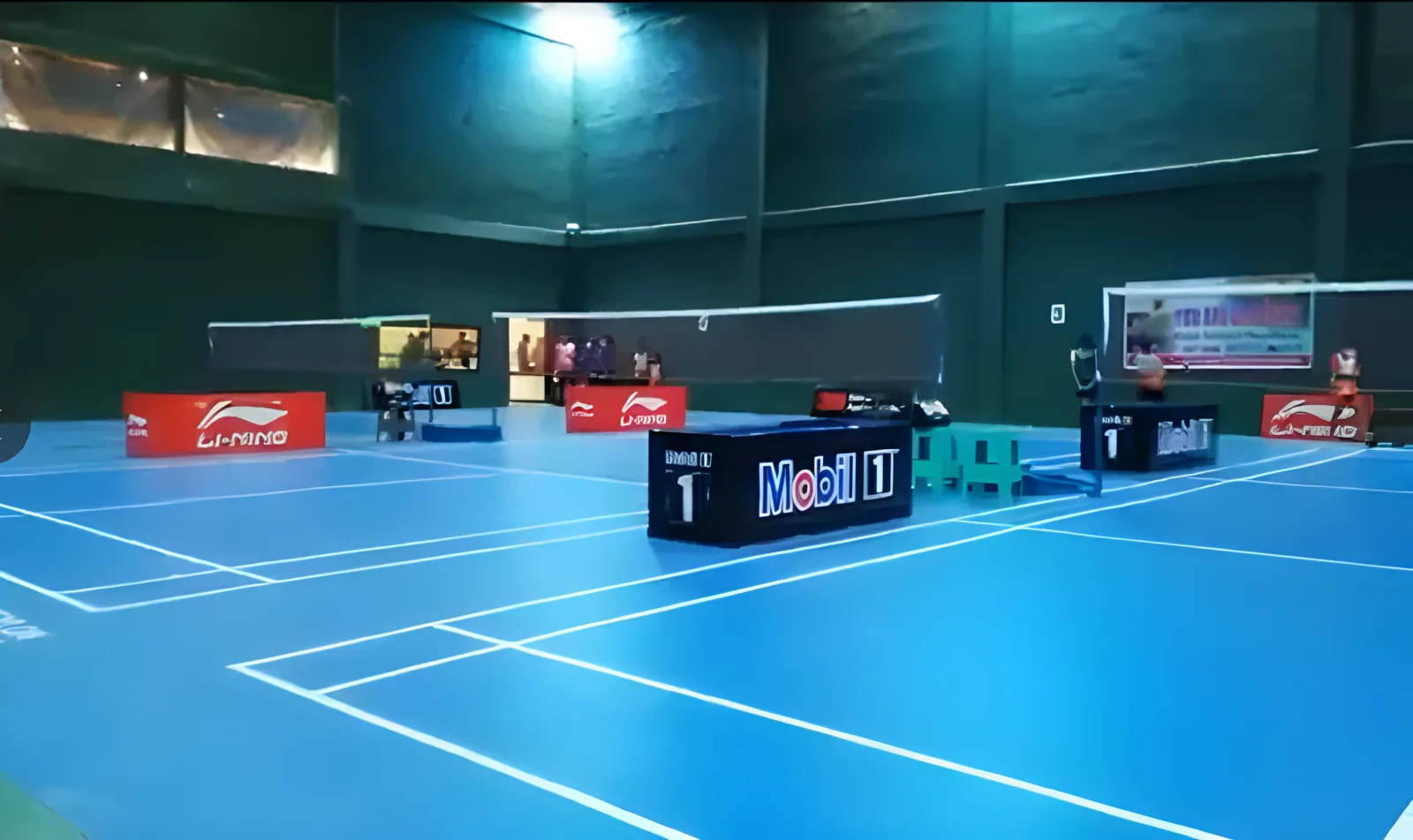 Blue synthetic badminton courts at Vishal Badminton Club, Kurunegala, with nets up, umpire chairs and Li-Ning boards along the side of the hall